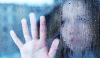 melancholy and sad young  woman  at the window in the rain